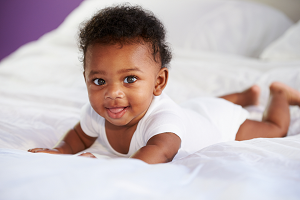 African American baby in white one piece on tummy with adorable smile.