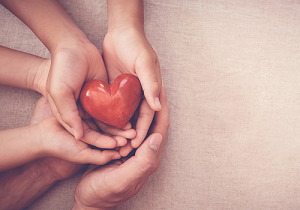 Hands holding a heart shaped stone.
