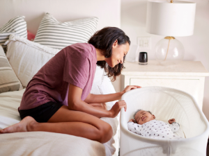 Image of women sitting on bed looking at baby in bassinet next to bed.